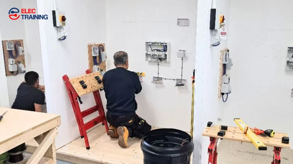 Adult learners practising electrical installations on training bays in a supervised workshop environment.