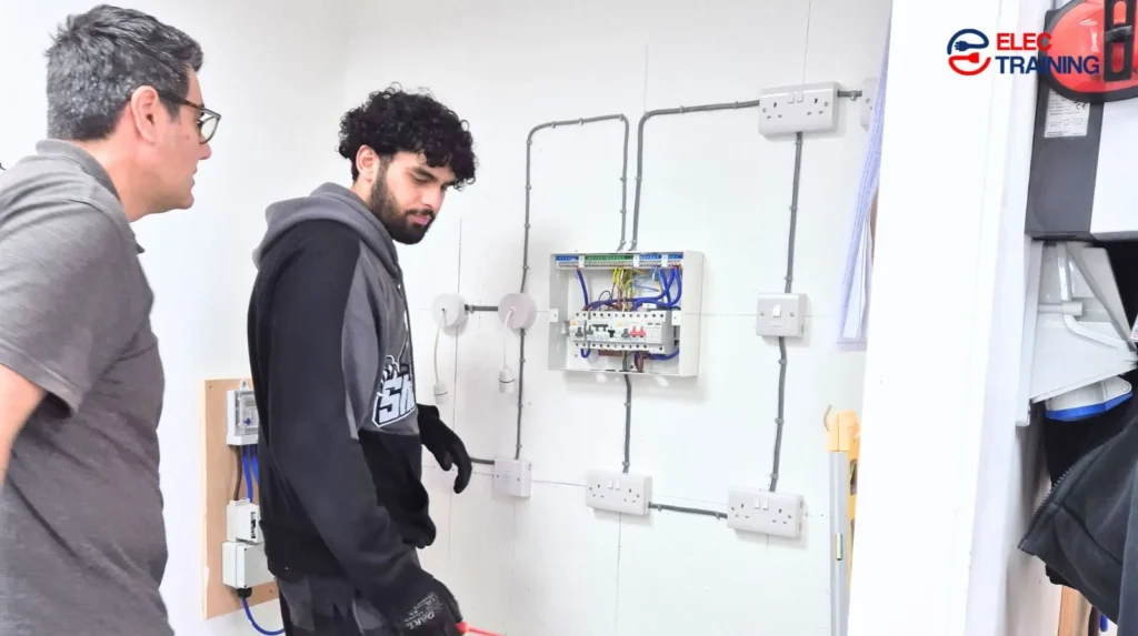 Adult trainee electrician gathering NVQ portfolio evidence on workplace installation with supervising qualified electrician